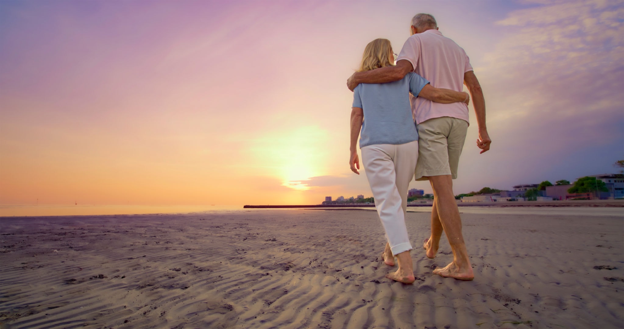 Older couple walking together on the beach at sunset