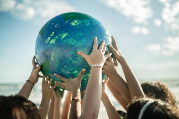 Diverse hands holding up a globe together against a blue sky